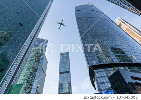 Modern glass skyscrapers on a clear day and passenger airliner fly over 137045008