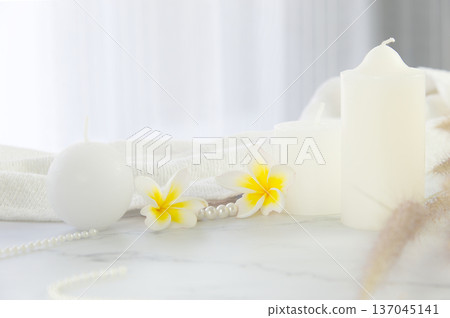 Luxury white stone marble tabletop in a bright room. Decorated with candle ,frangipani flower and white fabric with a blurred curtain of a window background for copy space 137045141