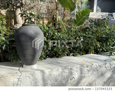 Earthenware pot on stone wall surrounded by lush greenery in outdoor garden setting Earthenware pot on stone wall surrounded by lush greenery in outdoor garden setting 137045325