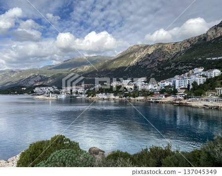 Coastal town with mountainous backdrop under cloudy sky, perfect for travel background or adventure 137045349