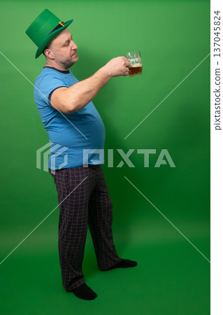 Man in green leprechaun hat toasting with beer glass. St. Patricks Day festive character embodying Irish holiday spirit and pub celebration tradition. photography 137045824