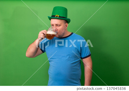 Man drinking beer while wearing green leprechaun hat. St. Patricks Day festive toast. Irish holiday celebration and pub tradition photography Man drinking beer while wearing green leprechaun hat. St. Patricks Day festive toast. Irish holiday celebration and pub tradition photography 137045836