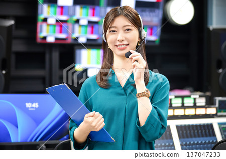 一位佩戴對講機的女製作人員面帶微笑地在攝影棚裡進行指令指示。拍攝合作：Sky Perfect 東京媒體中心 137047233