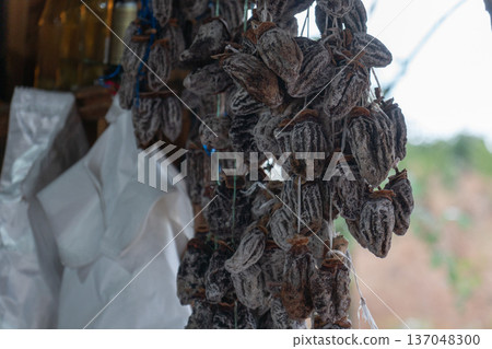 Dried persimmon fruits hanging in strings, close up view of natural preserved fruit with earthy brown tones and textured surfaces. Image supports food marketing, healthy snack promotion Dried persimmon fruits hanging in strings, close up view of natural preserved fruit with earthy brown tones and textured surfaces. Image supports food marketing, healthy snack promotion 137048300