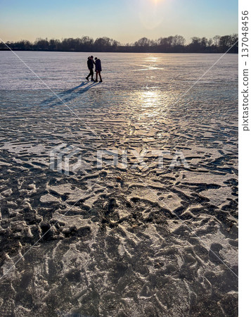 Two silhouettes on a frozen lake covered in footprints 137048456