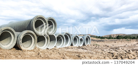 Large concrete pipes lie scattered on sandy ground beneath a dramatic sky, hinting at an ongoing construction project in a rural area, surrounded by nature Large concrete pipes lie scattered on sandy ground beneath a dramatic sky, hinting at an ongoing construction project in a rural area, surrounded by nature 137049204