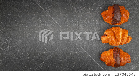 Three chocolate croissants on dark stone background, top view with copy space 137049543