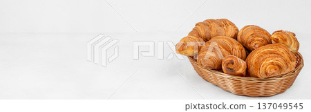 Assorted fresh croissants in wicker basket on light background Assorted fresh croissants in wicker basket on light background 137049545
