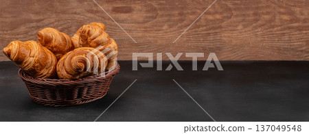 Fresh croissants in brown wicker basket on dark table 137049548
