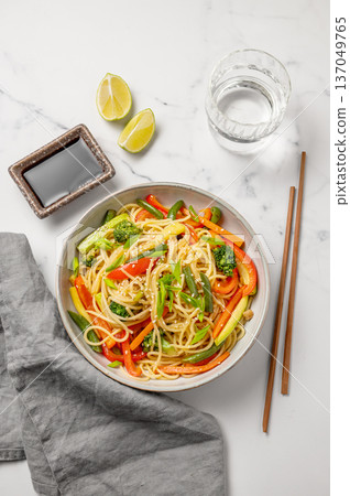 Stir fry wok noodles with vegetables in a plate on a light marble background with chopsticks Stir fry wok noodles with vegetables in a plate on a light marble background with chopsticks 137049765