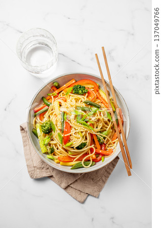 Vegetarian wok noodles with vegetables in a plate on a light marble background with chopsticks Vegetarian wok noodles with vegetables in a plate on a light marble background with chopsticks 137049766
