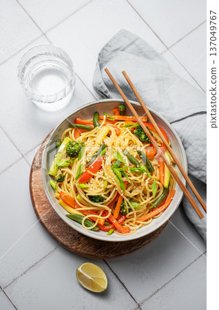 Stir fry wok noodles with vegetables in a plate on a gray kitchen tile background with chopsticks Stir fry wok noodles with vegetables in a plate on a gray kitchen tile background with chopsticks 137049767