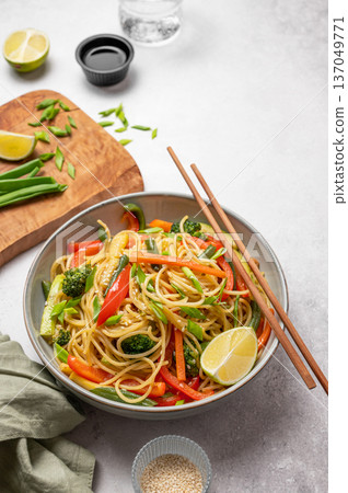 Stir fry wok noodles with vegetables in a plate on a light concrete background with chopsticks, soy sauce Stir fry wok noodles with vegetables in a plate on a light concrete background with chopsticks, soy sauce 137049771