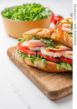 Two croissant sandwiches with ham, mozzarella cheese and arugula on a wooden board Two croissant sandwiches with ham, mozzarella cheese and arugula on a wooden board 137049782