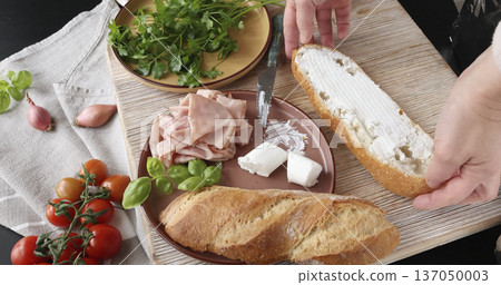 Anonymous person prepares sandwich with cheese, basil, and mortadella in kitchen. Italian cuisine, high-quality farm-to-table ingredients. 137050003