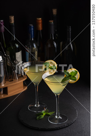 Elegant cocktail two glasses of limoncello spritz, garnished with fresh lemon slices and mint sprigs against a refined bar background with cocktail tools 137050480