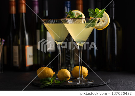 Elegant cocktail two glasses of limoncello spritz, garnished with fresh lemon slices and mint sprigs against a refined bar background with cocktail tools 137050482