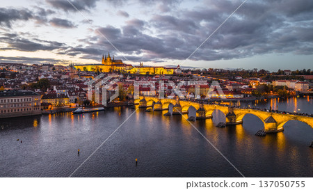 Prague Castle stands on the hill while Charles Bridge stretches over the Vltava River. The city lights glow as dusk settles, creating a scenic view of Czechia. Prague Castle stands on the hill while Charles Bridge stretches over the Vltava River. The city lights glow as dusk settles, creating a scenic view of Czechia. 137050755