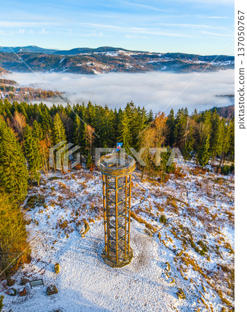 Svetly vrch lookout tower stands in Albrechtice, surrounded by snow and trees. The tower offers views of the mountains and the fog below. Visitors explore the area amid nature in winter. Svetly vrch lookout tower stands in Albrechtice, surrounded by snow and trees. The tower offers views of the mountains and the fog below. Visitors explore the area amid nature in winter. 137050767
