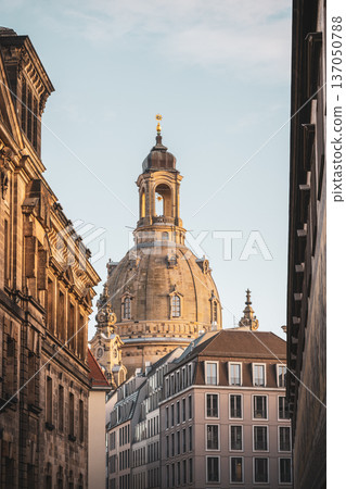 The Frauenkirche towers above the buildings in Dresden. The sun shines on the dome, highlighting its structure. This scene showcases the church against a clear sky during the winter season. The Frauenkirche towers above the buildings in Dresden. The sun shines on the dome, highlighting its structure. This scene showcases the church against a clear sky during the winter season. 137050788