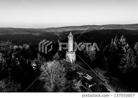 Visitors admire the Stepanka lookout tower in the Jizera Mountains during winter. The tower stands tall among trees as the sun sets behind distant hills. Visitors admire the Stepanka lookout tower in the Jizera Mountains during winter. The tower stands tall among trees as the sun sets behind distant hills. 137050807