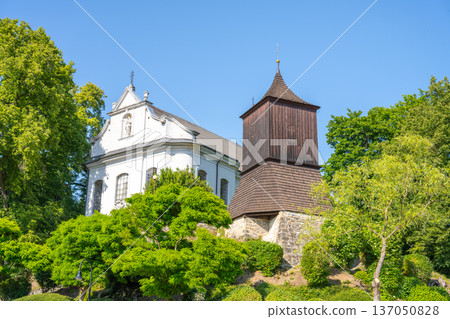 The Church of St. James the Greater stands in Zelezny Brod. It is surrounded by greenery and has a distinct tower. The sky is clear and the setting is bright and sunny. The Church of St. James the Greater stands in Zelezny Brod. It is surrounded by greenery and has a distinct tower. The sky is clear and the setting is bright and sunny. 137050828