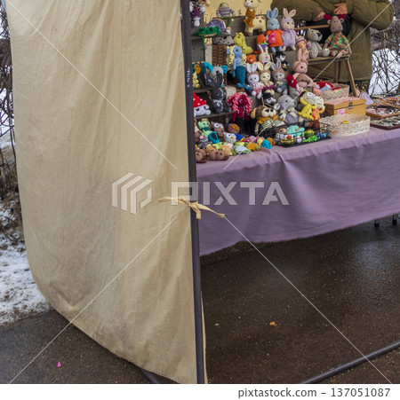 A stall at an outdoor market or craft fair featuring a collection of handmade plush toys, specifically crochet or knit dolls and animals. 137051087
