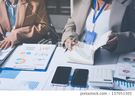 Business colleagues analyzing financial charts and reports on the table while having a focused discussion about strategies and market performance during an important meeting in a modern office setup 137051305