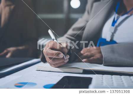 Business colleagues analyzing financial charts and reports on the table while having a focused discussion about strategies and market performance during an important meeting in a modern office setup 137051308
