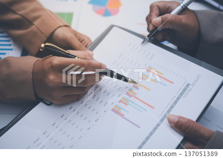 Business colleagues analyzing financial charts and reports on the table while having a focused discussion about strategies and market performance during an important meeting in a modern office setup 137051389