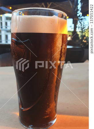 A refreshing glass of dark beer with thick foam stands on the table on a hot summer day 137051422