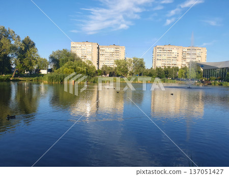 A sunny summer day in the city, where a quiet lake reflects the bright blue sky 137051427