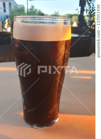 A refreshing glass of dark beer with thick foam stands on the table on a hot summer day 137051430