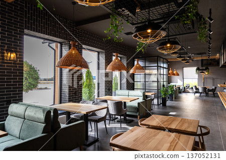 Modern restaurant interior with wooden tables and cozy seating near panoramic windows Modern restaurant interior with wooden tables and cozy seating near panoramic windows 137052131