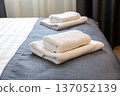 Folded white towels on hotel bed close up with clean modern hospitality interior 137052139