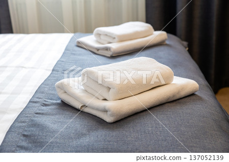 Folded white towels on hotel bed close up with clean modern hospitality interior 137052139