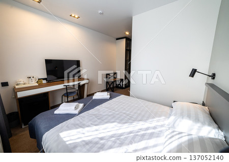 Cozy modern hotel bedroom with double bed fresh towels and soft natural window light Cozy modern hotel bedroom with double bed fresh towels and soft natural window light 137052140