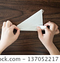 孩子的手在木桌上折一架銀色的摺紙飛機。 137052217