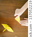 孩子的手正在用黃色摺紙折一隻鶴。 137052219
