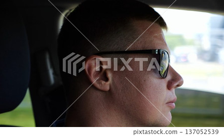 Profile of confident man driving a motor car at town. Male face of male driver in sunglasses looking concentrated to urban road while riding automobile. Slow motion Profile of confident man driving a motor car at town. Male face of male driver in sunglasses looking concentrated to urban road while riding automobile. Slow motion 137052539