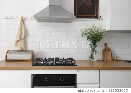 Modern eclectic kitchen interior. White metro tiles wall background. Old oil painting. Wooden countertop, stainless steel hood and gas stove. Scandinavian design. Home staging. Vase of cow parsley Modern eclectic kitchen interior. White metro tiles wall background. Old oil painting. Wooden countertop, stainless steel hood and gas stove. Scandinavian design. Home staging. Vase of cow parsley 137053625