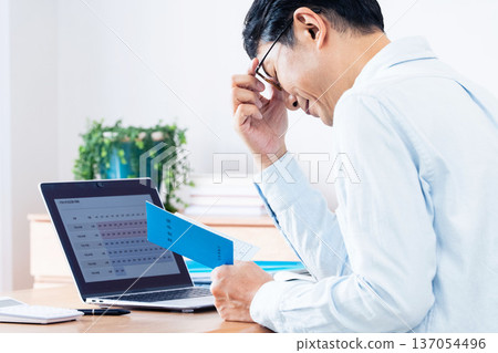 A middle-aged man thinking while looking at his pension book A middle-aged man thinking while looking at his pension book 137054496