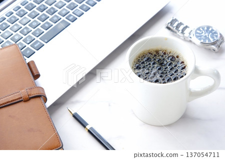 An image of someone working at a desk with a laptop and a personal organizer while drinking freshly brewed delicious coffee 137054711