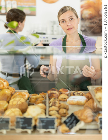 Adult woman putting pastries in display case in cafe Adult woman putting pastries in display case in cafe 137058261