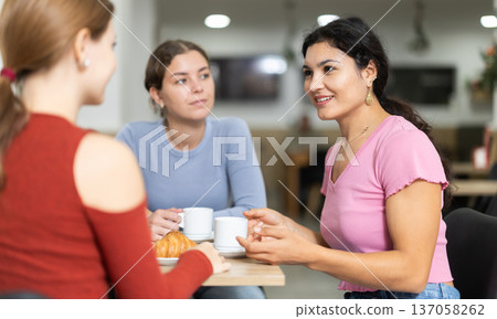 Three friends are chatting at table in cafe. They are drinking coffee or tea Three friends are chatting at table in cafe. They are drinking coffee or tea 137058262