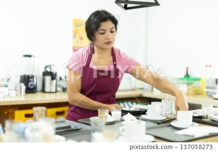 Cafe waitress clears dirty dishes from tables and takes them to the kitchen for washing. 137058273