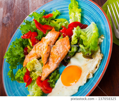 Image of plate with fried trout, egg, vegetables and green lettuce 137058325