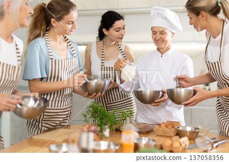Mature female cook holding bowl and milk pitcher Mature female cook holding bowl and milk pitcher 137058356