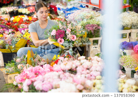 Cheerful girl choosing floral arrangement amidst flower market stalls Cheerful girl choosing floral arrangement amidst flower market stalls 137058360