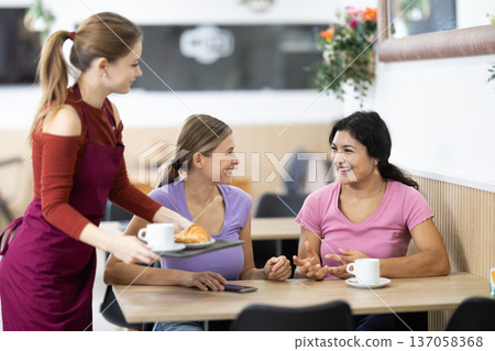 Girl waiter in apron presents coffee and croissants to restaurants guests. 137058368